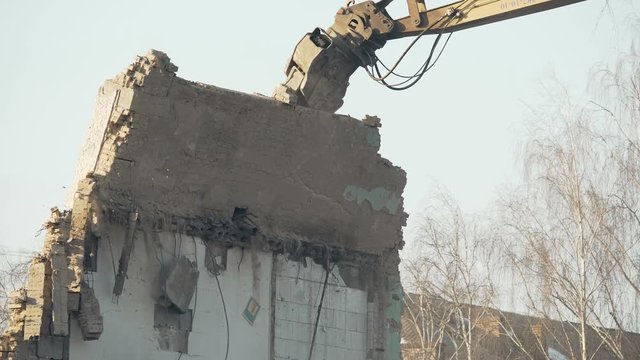Powerful excavator devastating remains of old ruined building, wall collapse