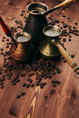 Hot coffee in group shabby antique turkish pots cezve with crema, beans with blur on brown old wooden board background, vertical shot. Rustic style.