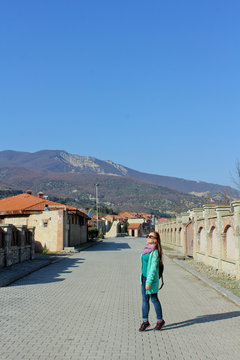 Traveler smile girl walking in the old town Mtskheta, Georgia. Sunny mountains at the background. Young traveler woman wearing sweater mint color and sunglass