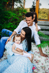 Lovely parents sit with their little girls on plaid outside