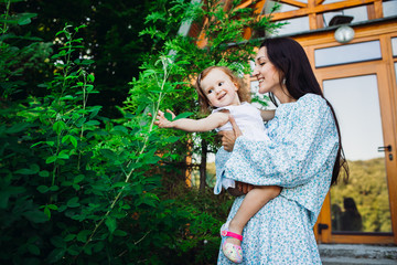 Cheerful woman holds her charming little daughter standing outside
