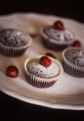 Hot sweet yummy chocolate cupcakes with powdered sugar and detail cherry on the top on the white plate on the table on smooth background