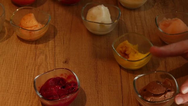 4K Close up of ice cream tasting - hand of a man dipping in scoops of ice-cream, blackcurrant, strawberry raspberry, lemon, mango and chocolate flavours