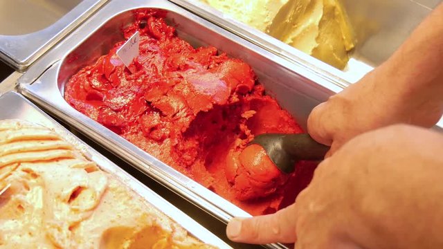 4K close-up of the hand of a man making a red scoop ice-cream, blackcurrant, strawberry and raspberry flavor.