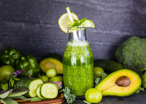 Healthy green smoothie in a glass bottle on dark stone background.