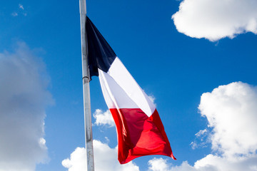 flag of France at half-mast in a blue sky with some clouds