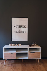 Coziness at home. Modern interior design. Chest of drawers with candles and minimalistic picture 'nothing is impossible' above it. Comfortable life, daily motivation concept.