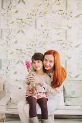 girl sitting in mom's on her knees. sniffing flowers