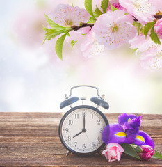 Spring time concept - retro alarm clock with fresh flowers on wooden shelf
