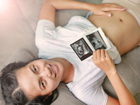 pregnant woman with ultrasound film lying on gray sofa at home, focus at her face