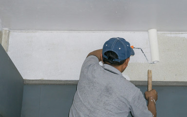 Painter man at work with a paint roller on the wall.