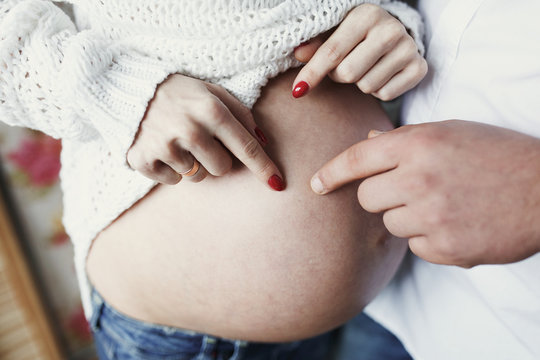 Man and woman with red nails touch with their fingers her pregnant belly