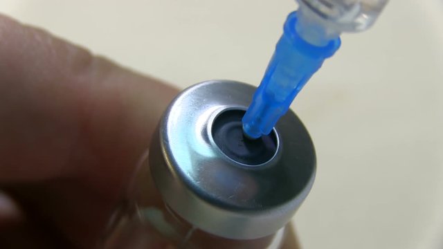Doctor With Syringe Needle Pierces The Rubber Stopper Of The Glass Ampoule With Medication Vial On A Light Background