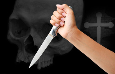 hand holding a knife ready to strike down against skull on black background