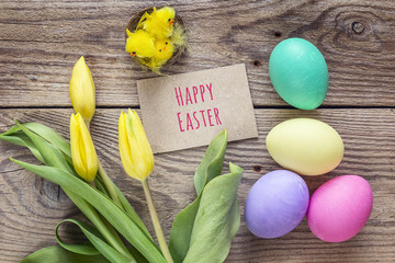 Message of Happy Easter, colored eggs, chickens and tulips on a old wooden table.