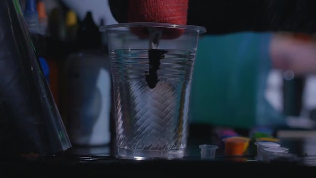 A tattooist mixing ink in a cup of water in a tattoo studio in slow motion