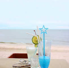 Glasses of beverage for two and eyeglasses on the table by the beach