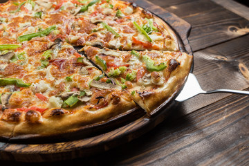Delicious pizza with mushrooms - thin pastry crust isolated at wooden background on wooden desk