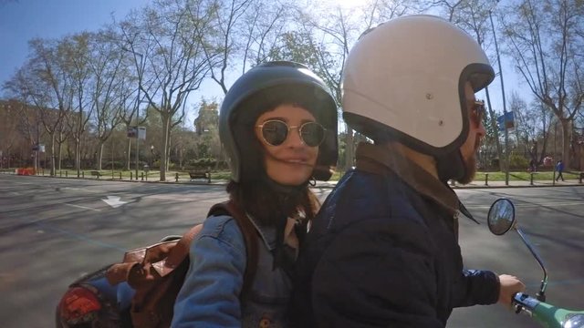 Lovely couple ride on mint electric scooter through empty summer city during their honeymoon adventure, attractive brunette girl smiles and takes selfie turning camera