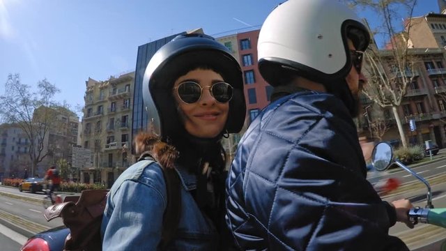 Lovely couple ride on rented electro scooter through traffic in summer city during their travel adventure, attractive brunette girl smiles and takes selfie turning camera around, looped video