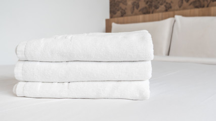 Three white laundered fluffy towels on white bed in bedroom interior at the hotel