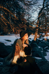 Portrait of a young beautiful blonde woman with hat, in a fur coat, outside, on the snow. A good dark day with beautiful shadows - a sunny winter day, sunset.