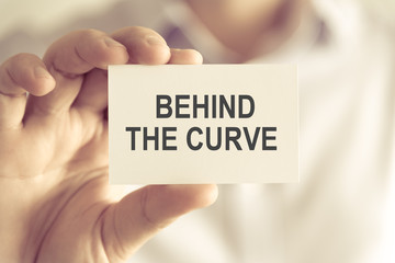 Businessman holding BEHIND THE CURVE message card