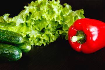Fresh vegetables on the table: red pepper, lettuce, cucumber. Dark background