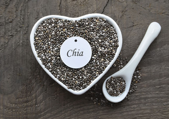 Chia seeds in a white heart shaped bowl on old wooden background.Salvia hispanica seeds.Healthy food or superfood concept.Selective focus.