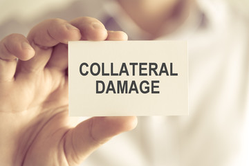 Businessman holding COLLATERAL DAMAGE message card