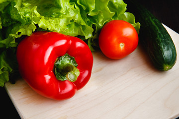 Fresh vegetables on the table: red pepper, lettuce, cucumber, tomatoes. Cutting board