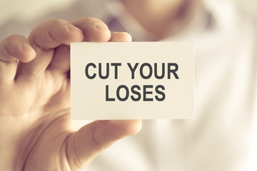 Businessman holding CUT YOUR LOSES message card