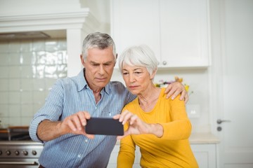 Obraz premium Senior couple taking selfie from mobile phone in kitchen