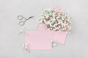 Mockup of gypsophila flowers in envelope and pink paper card on light table top view in flat lay...