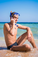 A young man sitting on the beach in the mask for diving