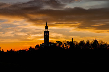 Naklejka premium Evening sunset with black silhouette of small church and bell tower and trees on colorful flaming cloudy sky background.
