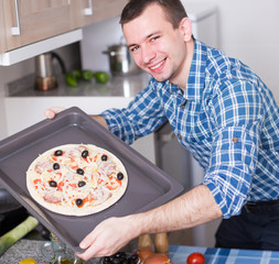 Young man preparing delicious pizza in oven