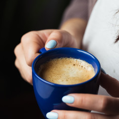 Girl with blue manicure holds a blue cup of coffee