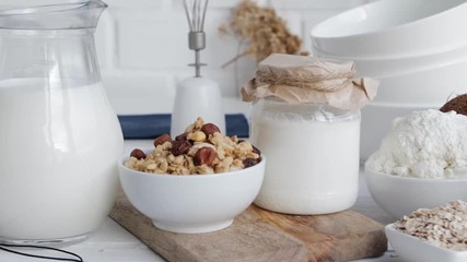 Piece of kitchen interior. Dairy products, eggs, cereals, on wooden table - milk, cottage cheese, sour cream, yoghurt, granola, muesli. Concept of healthy eating. Slow pan. - Powered by Adobe