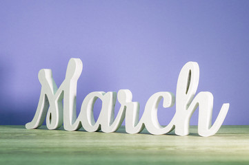 March - biginning of springtime concept. Wooden carved inscription on purple or dark pink background - Powered by Adobe