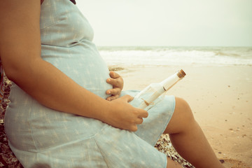 Fototapeta na wymiar a pregnant woman on the beach, her hand holding a bottle with a message inside.