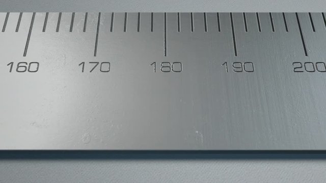 A close up pan along a section of a steel ruler with indented measurements on a white studio background