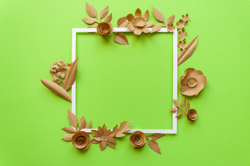 square frame with craft paper flowers on the green background. Flat lay. Nature concept