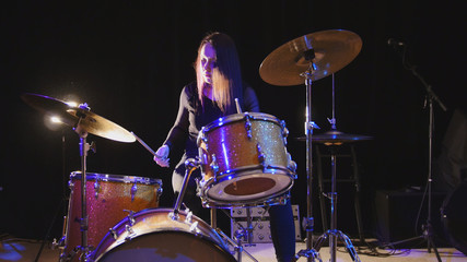 Fototapeta na wymiar Emotional girl drummer, attractive youngblack hair model plays the drums