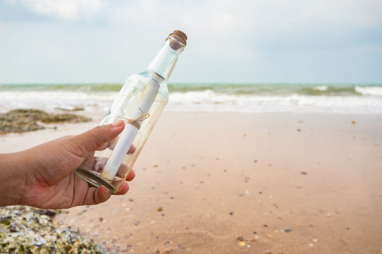 Hand holding bottle with a message on beach.