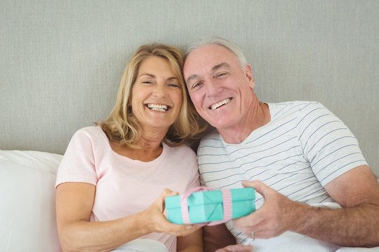 Senior couple holding gift box on bed