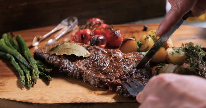 Cutting a slice of a delicious sirloin steak with asparagus, potatoes and roasted tomatoes
