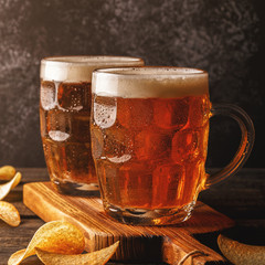Cold beer in glass with chips on a dark background.