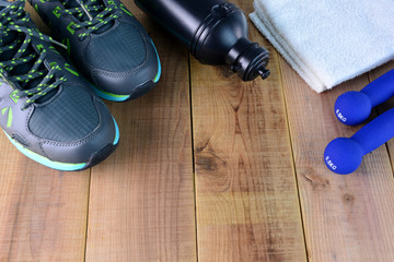 Sport shoes and towel, dumbbell, bottle of water on wooden.