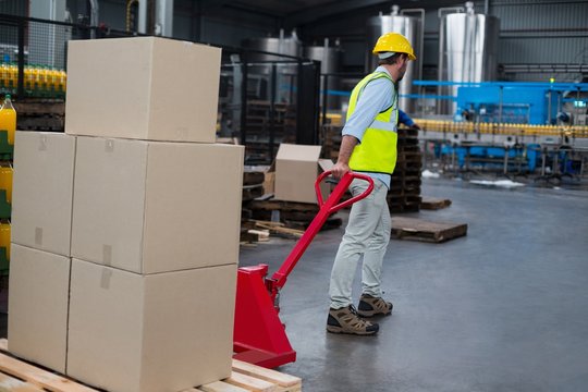 Factory worker pulling trolley of cardboard boxes